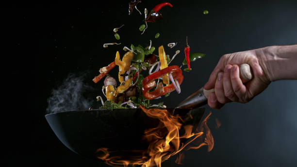 Freeze Motion of Wok Pan and Flying Ingredients in the Air. Freeze Motion of Wok Pan with Flying Ingredients in the Air and Fire Flames. slow motion stock pictures, royalty-free photos & images