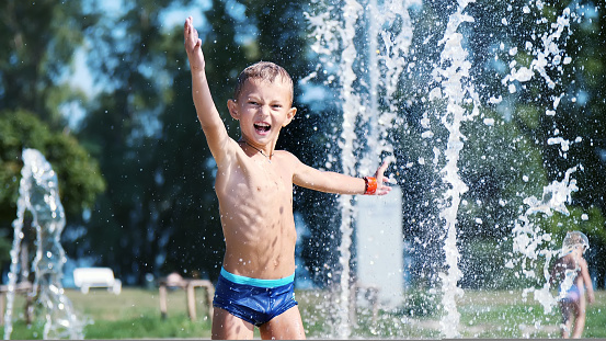 excited boy of seven years having fun between water jets, in fountain, run around, sprinkle, have fun, have fun, on a hot summer day. Summer in the city. Slow motion. High quality photo