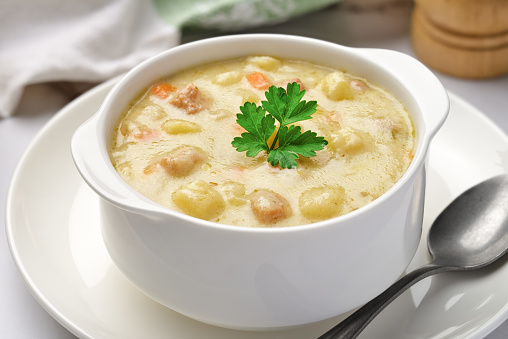 Close-up of a bowl of potato soup with vegetables and pieces of meat. Studio shot from a high angle.