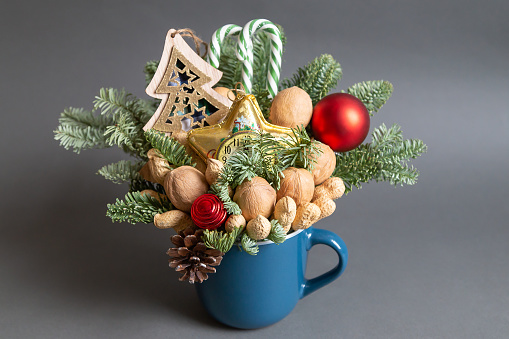 Christmas edible composition with nuts, sweets, nobilis and christmas decor in a blue cup on a gray background