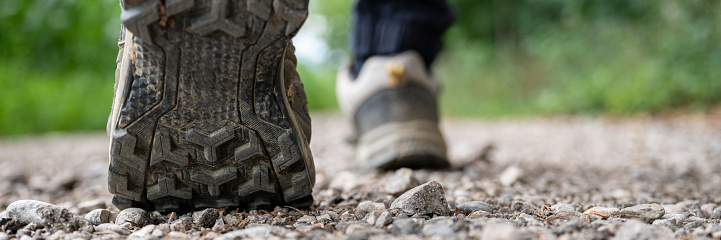 Closeup wide view image of male feet in hiking shoes walking on a gravel path in nature.