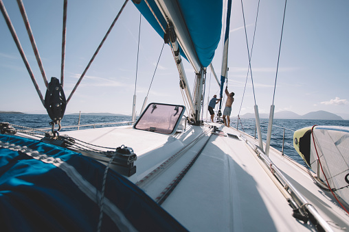 Two crew members pulling the rope, setting up sails on sailboat