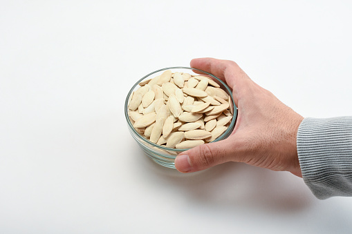 A hand holding bowl of pumpkin seeds on the white background