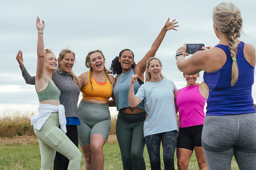 A front-view shot of a group of female friends outdoors on a field in Northumberland, England. They are taking a group picture on a smartphone.