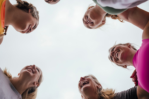 A low angle shot of a group of female friends standing in a circle outdoors on a field in Northumberland, England. They are preparing for a run in a huddle.