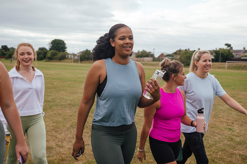 A side-view shot of a group of female friends walking outdoors on a field in Northumberland, England. They are preparing for a run.