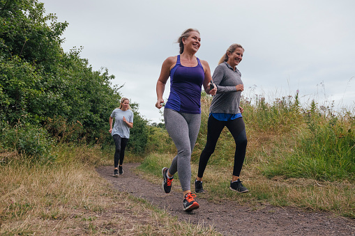 A side wide-view shot of a group of female friends running outdoors by a field in Northumberland, England.