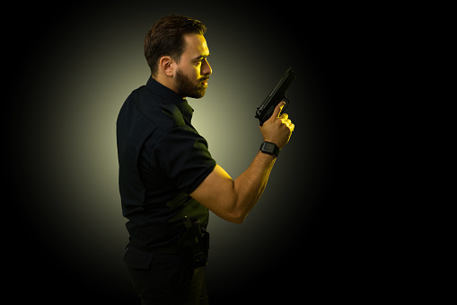 Profile of a police agent on duty using his gun while trying to catch and arrest a criminal