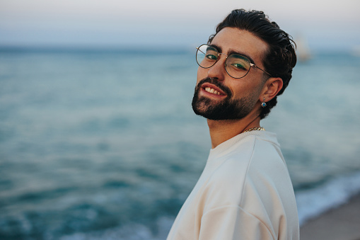 A portrait of a young and handsome Caucasian man posing for the camera at the beach, smiling and enjoying the sunset.
