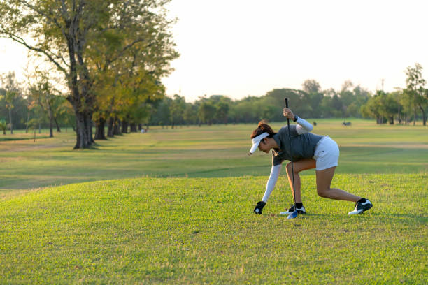 asian sporty woman putt golf ball on tee off with club in golf course on evening on time for healthy sport sunset background. lifestyle and sport concept - golf golf swing putting cheerful imagens e fotografias de stock