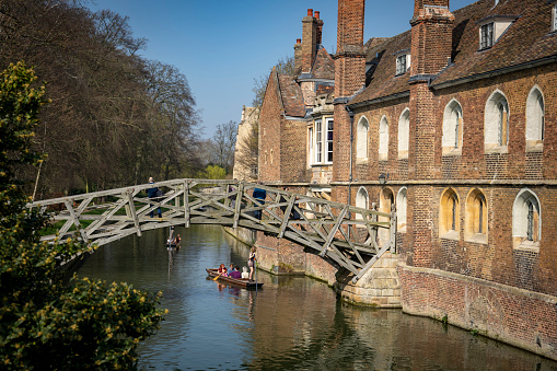 Punting on the River Cam with a punt going under the mathematical bridge in the foreground. Cambridge, Cambridgeshire, England, UK.