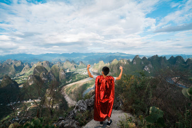 Young superhero showing muscles at mountain peak