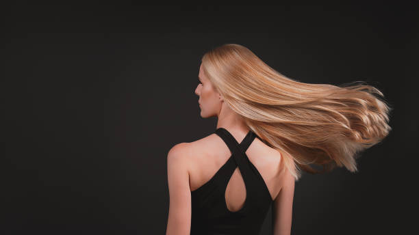 Beautiful, seductive blonde woman on dark background. Shiny golden healthy hair waving on wind. stock photo