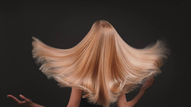 Beautiful, seductive blonde woman on dark background. Tossing shiny golden healthy hair. stock photo