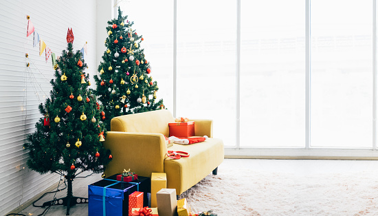 Living room with yellow sofa over carpet decorated with Christmas tree with gifts for the new year. Home and apartment interior decoration during the Christmas holiday. Image with copy space.