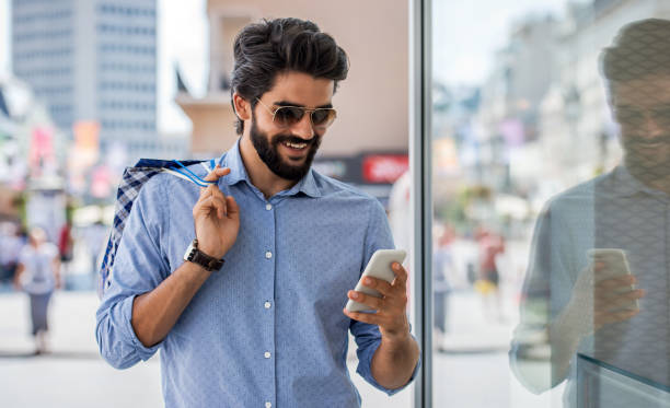 Smiling man using mobile phone during the shopping in the city. Consumerism, lifestyle concept stock photo
