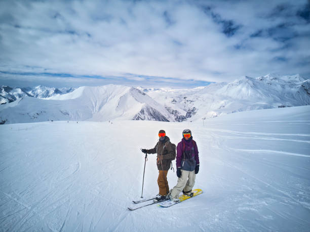 sciatore e snowboarder in piedi sulla cima della montagna contro il cielo blu e il panorama delle montagne. due amici attivi hanno vacanze sul concetto di stazione sciistica. foto aerea. - snowboarding friendship snow winter foto e immagini stock