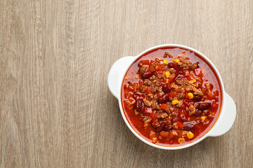 Bowl with tasty chili con carne on wooden table, top view. Space for text