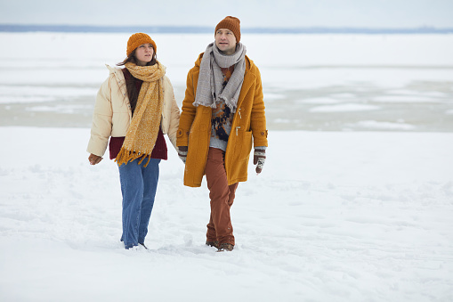 Full length portrait of young couple holding hands and walking towards camera in minimal winter landscape, copy space