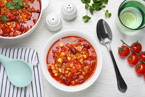 Tasty chili con carne served on white wooden table, flat lay