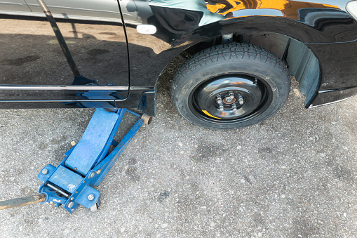 Hydraulic car jack lift car to replace punctured tyre with temporary emergency replacement tyre at road side