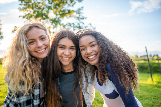 Summer Friendship A small group of three female friends huddle in closely together as they pose for a portrait.  They are each dressed casually and are smiling on the warm summers evening. happy young teens stock pictures, royalty-free photos & images