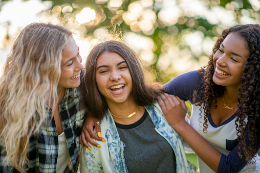 A small group of three female friends huddle in closely together as they pose for a portrait.  They are each dressed casually and are smiling on the warm summers evening.