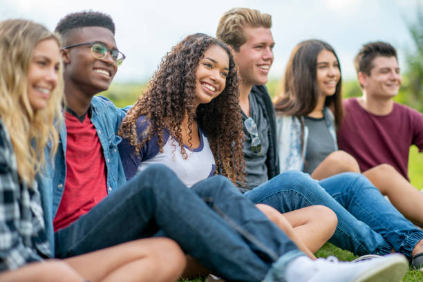 Teenagers Hanging Out Outside A small group of teenagers sit in the grass as they hang out talking and enjoying a few laughs together. They are each dressed casually and are smiling as they enjoy the fresh air. secondary school activities stock pictures, royalty-free photos & images