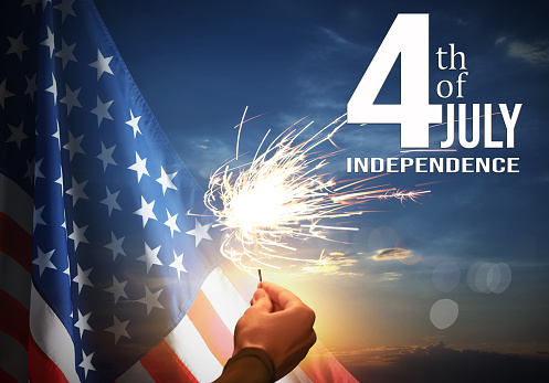 4th of July - Independence Day of USA. Woman holding burning sparkler near American flag outdoors at sunset, closeup