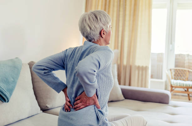 여자는 허리 통증을 느끼고, 아픈 근육을 마사지합니다. 거실에서 아프면서 아침 불편 함을 느끼는 성숙한 여성. - back rear view backache posture 뉴스 사진 이미지