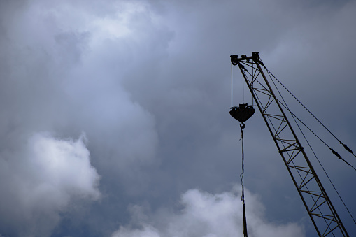 Silhouette of boom high rise crane against background clouds and dramatic sky