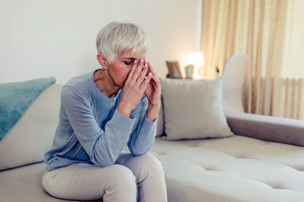 istock Sad depressed woman at home sitting on the couch, looking down and touching her forehead, loneliness and pain concept 1434436697