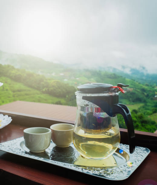 The breakfast tea set features two white ceramic mugs and a mug with a mountain in the background and a flare. stock photo