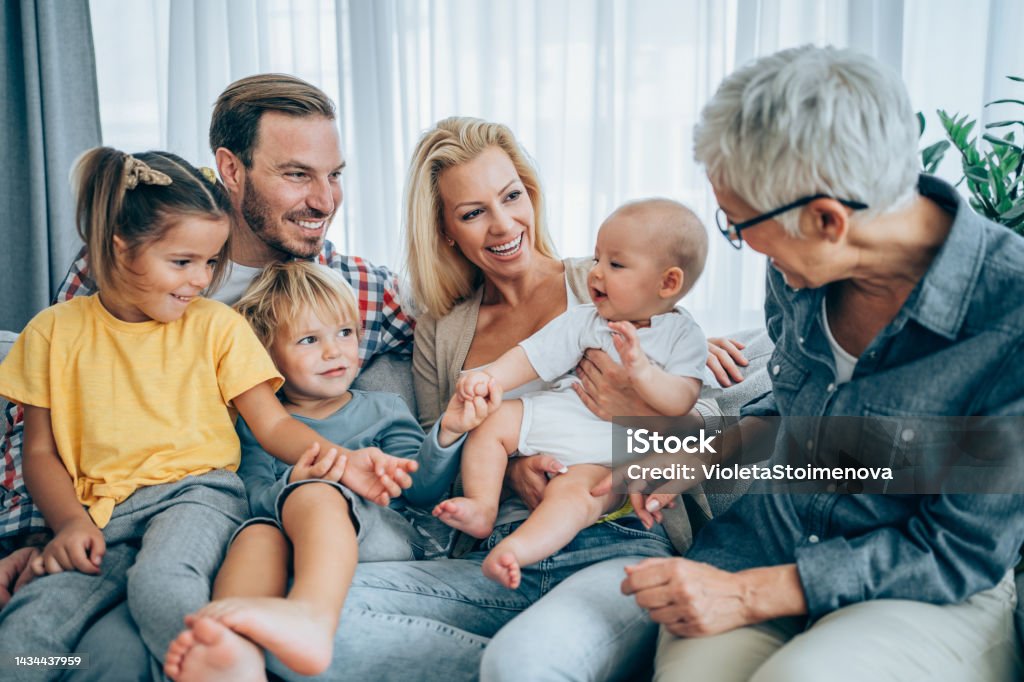 Happy family at home. Shot of three generations family relaxing together at home. Cheerful parents having fun while playing with their three kids on sofa in the living room. Multi-Generation Family Stock Photo