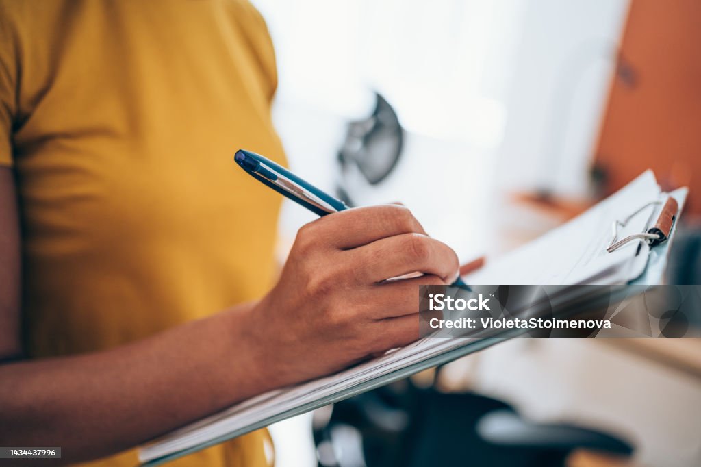 Woman hand writing on clipboard with a pen. Cropped shot of an unrecognizable businesswoman making notes on a clipboard inside of the office. Checklist Stock Photo