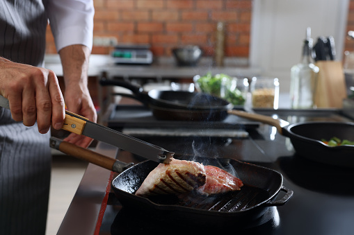 Professional chef cooking meat on stove in restaurant kitchen, closeup