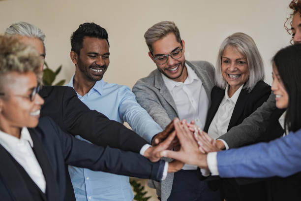 istock Group of multi generational business people celebrating success while stacking hands inside modern office 1434444236
