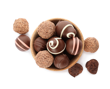 Bowl with many different delicious chocolate truffles on white background, top view