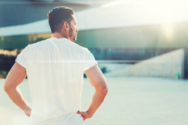 Back view of strong powerful runner looking away and thinking about workout in bright day in open square in sunlight