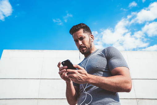 Confident strong caucasian male athlete checking updates of smartphone fitness app result while training outdoors keeping shape,millennial sportsman share publication about healthy lifestyle in blog