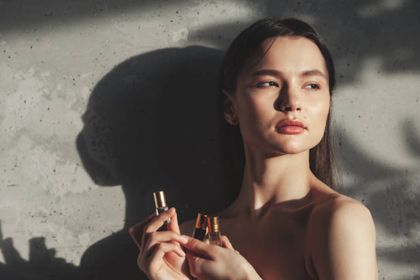 Woman holding hands perfume cosmetics bottle for applying drops to skin or hair. Lady with cologne at old wall background in foliage shadow. Concept of healthy lifestyle and self care. Copy text space mujer cogida de la mano frasco de cosméticos de perfume para aplicar gotas en la piel o el cabello. señora con colonia en el fondo de la pared vieja en la sombra del follaje. concepto de estilo de vida saludable y autocuidado. copiar espacio de texto