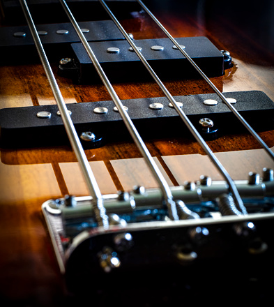 A close up macro type shot of a bass guitar. sunburst, with just strings and pick up showing