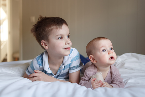 Portrait of a boy and baby girl lying on the bed at home and looking away