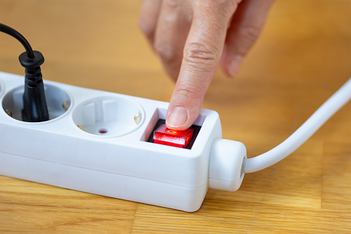 Pressing red button of a white power strip on wooden background - energy saving