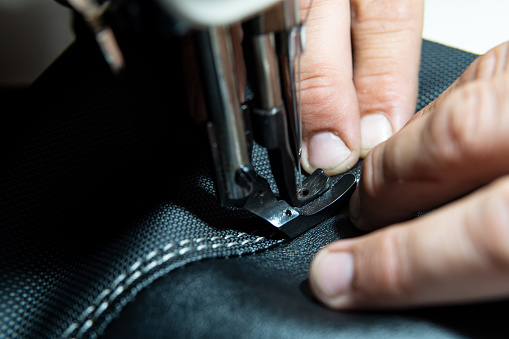 Close up view of Upholsterer's hands sewing leather parts with a sewing machine to fix a seat.