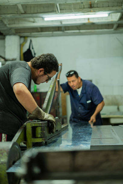 Casually dressed Latin men employed by a locksmith are inside their workplace making cuts of metal materials
