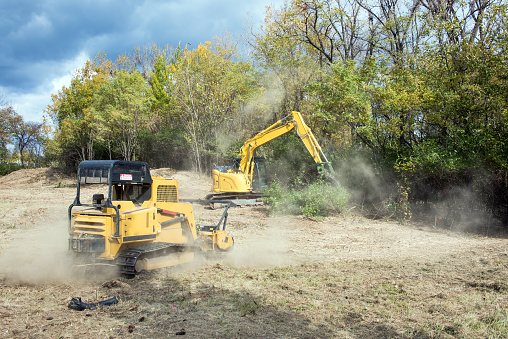 Forestry mulcher and backhoe machinery clearing parcel of land for development.