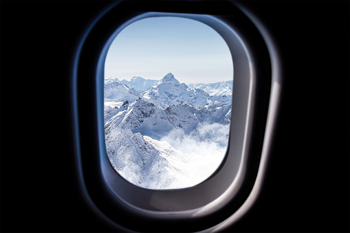 Mountains view through a jet plane window high on the blue sky