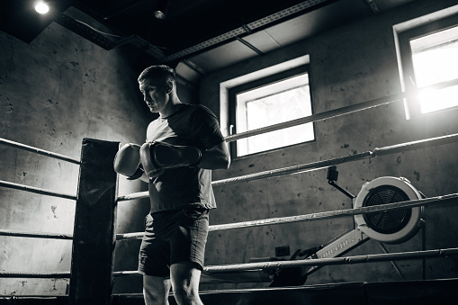 One man, handsome male boxer training alone in fighting ring.