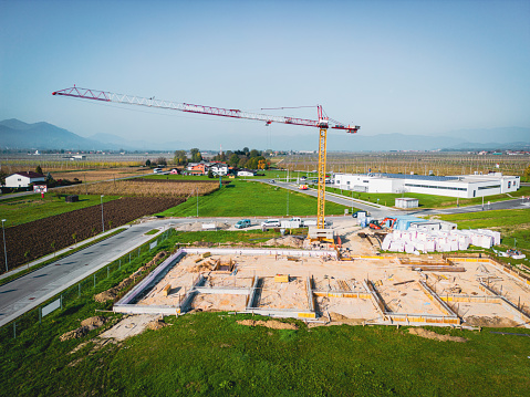 Aerial view of a building construction site in progress with tower crane, scaffolding, formwork, construction materials, equipment, reinforcing steel bars.
